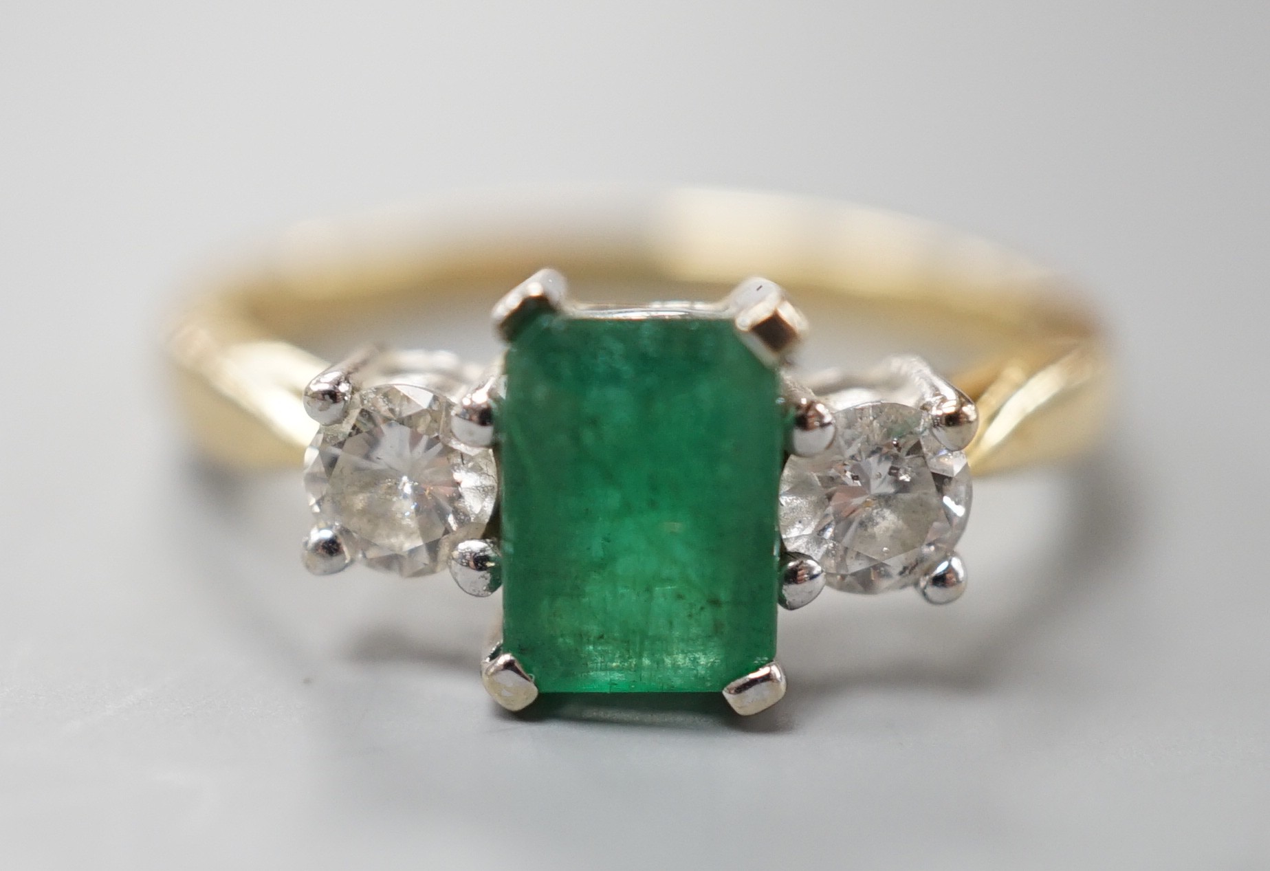 A modern 18ct gold, emerald and diamond set three stone ring, size N, gross weight 3.5 grams.